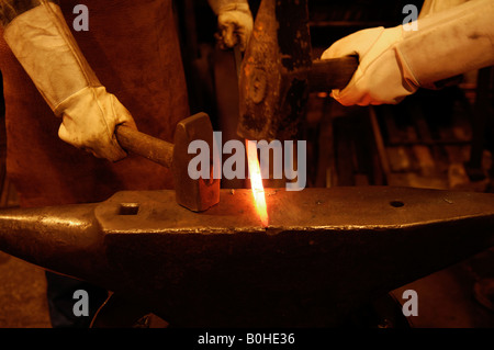 Glühende Eisenstange gehämmert in Form gegen einen Amboss durch zwei Schmiede tragen lange weiße Lederhandschuhe, Industriemuseum, Stockfoto