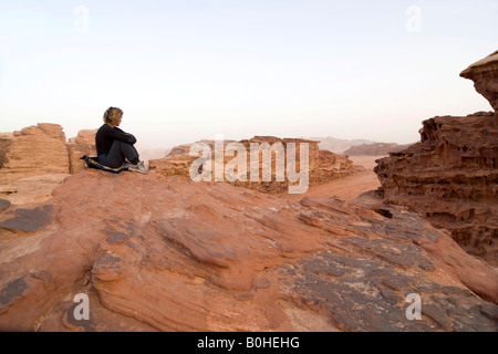 Frau sitzt auf eine Rock Ledge aussehende aus in der Entfernung, Wadi Rum, Jordanien, Naher Osten Stockfoto