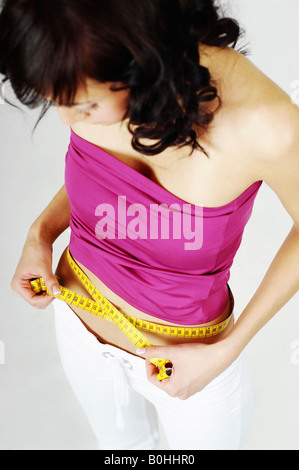 Junge Frau, die ihre Taille mit Maßband, Taillenumfang messen Stockfoto