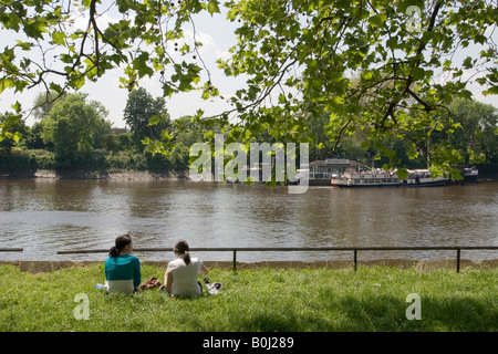 Zwei junge Mädchen an der Themse im The Strand auf der grünen Chiswick in der Frühlingssonne sitzen und Essen zu Mittag Stockfoto