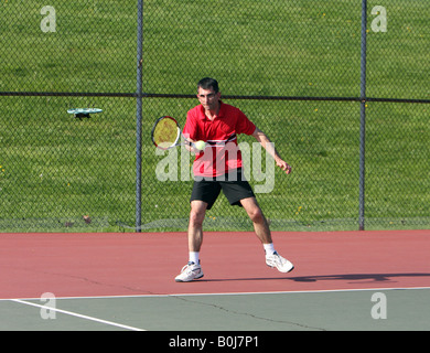 Ein junger Mann in einem roten Hemd mit dem Tennisspielen. Stockfoto