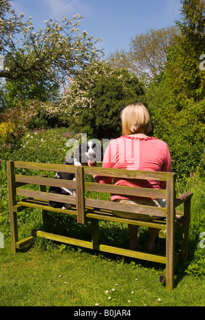 Frau sitzt im englischen Cottage-Garten mit ihrem English Springer Spaniel im Frühjahr Stockfoto