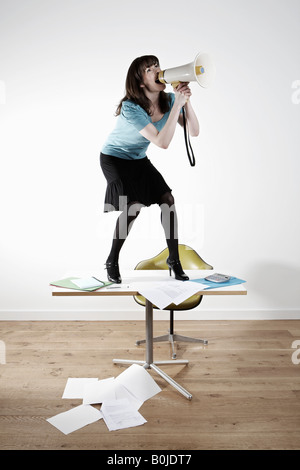Frau stehend auf Schreibtisch, schreien über Megaphon Stockfoto