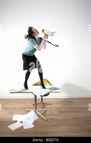Frau stehend auf Schreibtisch, schreien über Megaphon Stockfoto