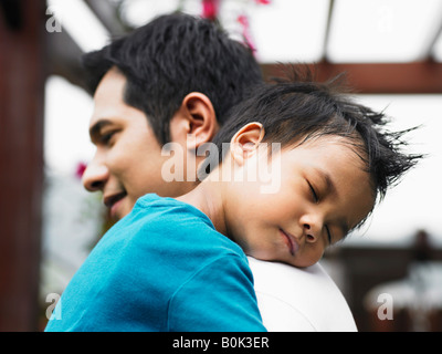 Junge Augen geschlossen, auf Vaters Schulter Stockfoto