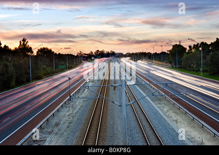 Verkehr auf dem Mitchell Freeway bei Sonnenuntergang. Ein Gleis liegt zwischen der Straße. Leederville, Perth, Western Australia, Australia Stockfoto