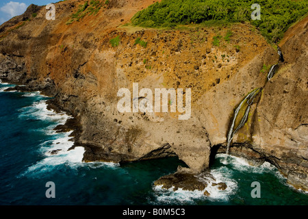 Brandung gegen die Felsen und schmalen Wasserfall hinunter läuft felsige Klippe in den Ozean von einem großen Rock arch an der Nordküste von Kauai Ufer, die NaPali Küste. Stockfoto