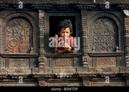 Eine Mädchen lehnt sich aus dem Fenster ihres schön geschnitzten Hauses, Gatlang, Tamang Heritage Trail, Nepal Stockfoto