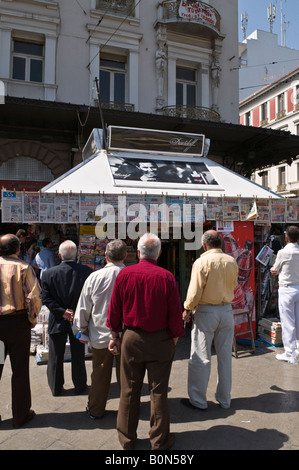 Leute lesen die Schlagzeilen auf Zeitungen oberhalb einer Periptero News-Kiosk in Omonia-Platz, Athen, Griechenland Stockfoto