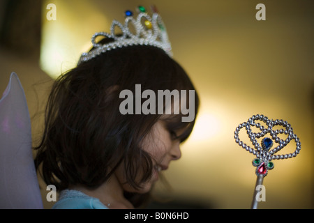 Vier Jahre altes Mädchen in Fee Kostüm noch ihren Schlafanzug trägt sie setzt auf die Flügel Tiara und nimmt den Zauberstab Stockfoto