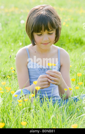 junge weibliche Kind Schneidersitz sitzen in einem Feld voller Butterblumen Stockfoto