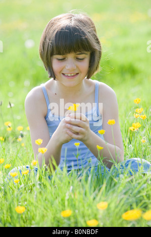 junge weibliche Kind Schneidersitz sitzen in einem Feld voller Butterblumen lächelnd Stockfoto