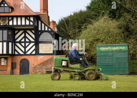 Mann sitzt auf motorisierten Rasenmäher mäht Cricket Pitch Rasen am Dorfplatz von Institutsgebäude Tilford Surrey England UK Stockfoto