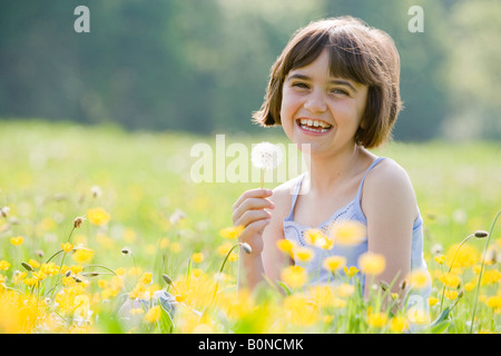 junge weibliche Kind Schneidersitz sitzen in einem Feld voller Butterblumen holding Löwenzahn und lächelt in die Kamera mit Platz für Kopie Stockfoto