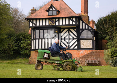 Mann sitzt auf motorisierten Rasenmäher mäht Cricket Pitch Rasen am Dorfplatz von Institutsgebäude Tilford Surrey England UK Stockfoto