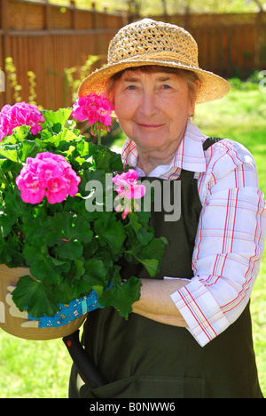 Ältere Frau hält einen Topf mit Blumen in ihrem Garten Stockfoto