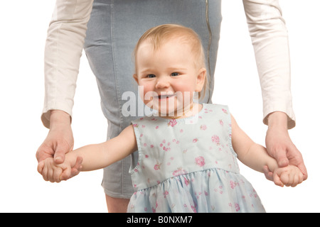 Das lächelnde Mädchen in einem blauen Kleid halten auf Mama s Hände und versucht, zu gehen Stockfoto