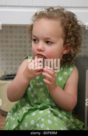 Eine kleine 2 jährige Mädchen Kleinkind ein Schokoladenei in der Küche Junk-Food Essen Stockfoto