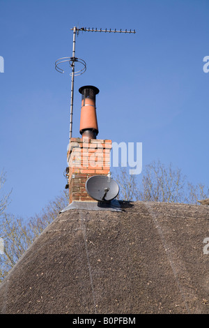 Satellitenschüssel auf einem Strohdach neben einem Schornstein montiert TV Ariel Antenne. Stockfoto