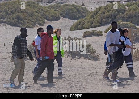 Illegale Einwanderer aus Afrika landen an einem Strand auf Teneriffa auf den Kanarischen Inseln und erhalten Hilfe vom Roten Kreuz. Stockfoto