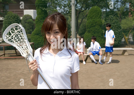 Teenager-Mädchen stehen und hält Lacrosse Stock mit Freunden sitzen auf Bank im Hintergrund, Porträt