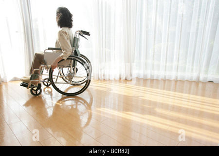 Ältere Frau auf Rollstuhl Blick durch Fenster Stockfoto
