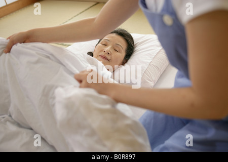 Krankenschwester stopfte senior Frau im Bett im Pflegeheim Stockfoto