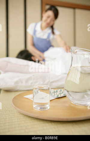 Wasser Krug und Medizin Pillen auf Tablett mit senior Frau Matratze auflegen und Krankenschwester auf Hintergrund Stockfoto