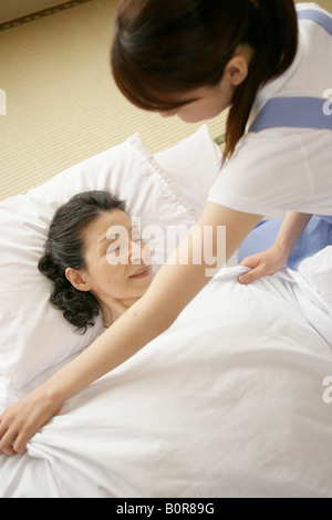 Krankenschwester stopfte senior Frau im Bett im Pflegeheim Stockfoto