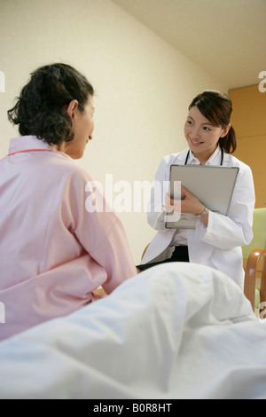 Ärztin im Gespräch mit älteren Frau sitzt am Krankenhausbett Stockfoto