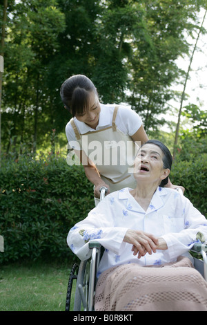 Krankenschwester, die Unterstützung der älteren Frau im Rollstuhl im Garten Stockfoto