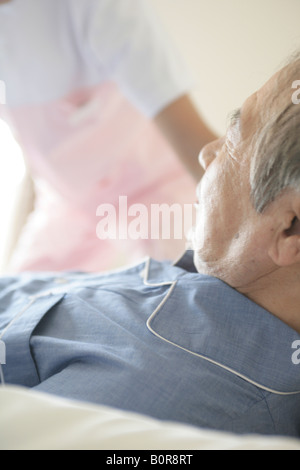 Älteren Mann im Bett liegend, Krankenschwester im Hintergrund Stockfoto