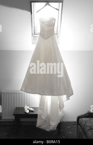 Ein Brautkleid hängen im Fenster des Hotelzimmers die Braut vor ihrer Hochzeit. Stockfoto