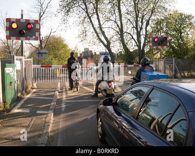 Motorräder und Fahrräder warten an einer Eisenbahn Bahnübergang Schranke, bevor ein Zug über den Grenzübergang passiert. Stockfoto