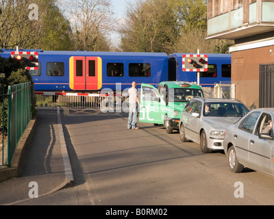 Fahrzeuge warten auf eine zweite Bahn Bahnübergang Barriere wie durchläuft die erste Durchquerung trainieren & als ein Taxifahrer Uhren. Stockfoto