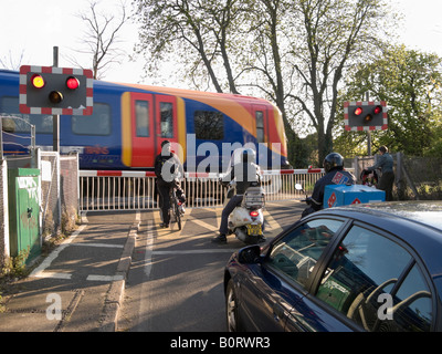 Motorräder und Fahrräder warten auf eine Eisenbahn Bahnübergang Barriere während der Überfahrt Bahn durchläuft. Stockfoto