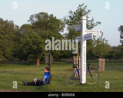 Fahrradfahrer entspannt durch gelehnt ein Wegweiser in der Nähe von Richmond Tor im Richmond Park, Surrey. UK Stockfoto