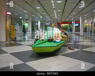 Passagiere schlafen auf Bänken, während sie auf ihren Flug im Münchner Flughafen Terminal Deutschland warten Stockfoto