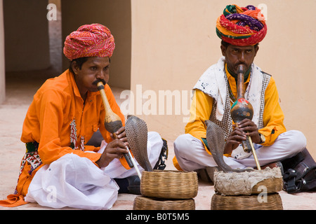 2 Traditionell gekleidete Schlangenbeschwörer spielen ihre Flöten für 2 aufmerksamen Königskobras aus Körbe im Innenhof des Fort Amber in Rajasthan, Indien Stockfoto