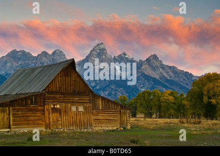 Rosa Wolken bei Morgendämmerung über alte hölzerne Scheune Berge und Bäume im Herbst entlang Mormone Zeile Grand Teton Nationalpark Wyoming Stockfoto