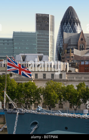 Der Union Jack Flagge fliegt auf dem Deck der HMS Belfast die Willis und Gherkin Gebäude sind sichtbar in der City of London Stockfoto