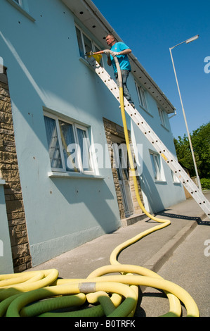 Mann auf Leiter installieren Hohlwand Steinwolle in einem Haus zur Verbesserung der Energieeffizienz und Reduzierung der Heizkosten Stockfoto