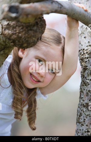 Fünf Jahre altes Mädchen lächelt in die Kamera stehend neben einem Baum. Stockfoto