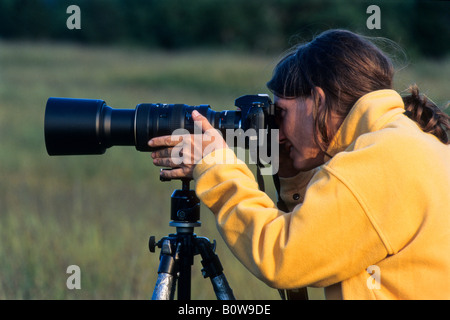 Fotografin trägt eine gelbe Jacke, eine Aufnahme mit Kamera, Stativ, Teleobjektiv Stockfoto