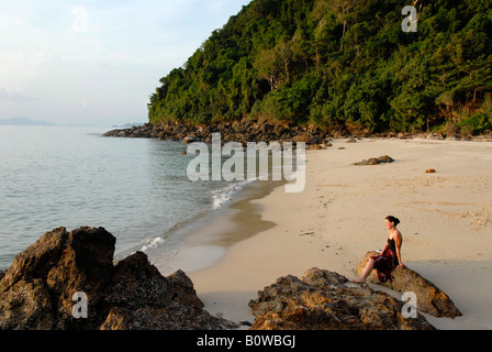 Junge Frau sitzt alleine auf einem Felsen an einem leeren Strand, Koh Kradan, Thailand, Südostasien Stockfoto