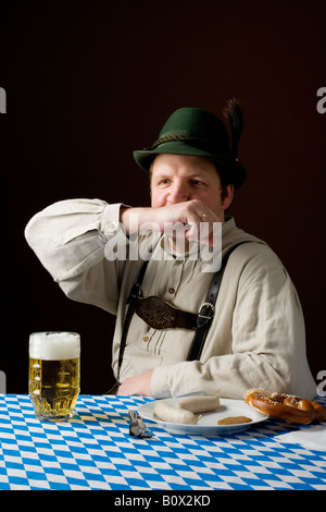 Stereotype deutscher Mann in bayrischer Tracht Mund abwischen, an einem Tisch mit einem Bier und deutsches Essen Stockfoto