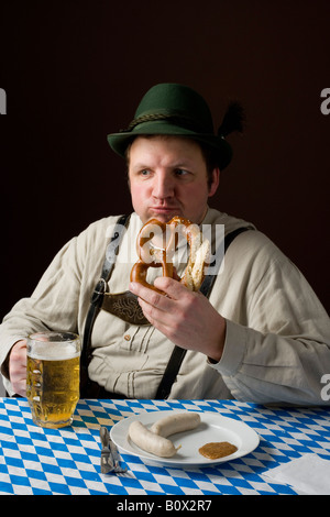 Stereotype deutscher Mann in bayrischer Tracht eine Brezel zu essen und ein Bier trinken Stockfoto