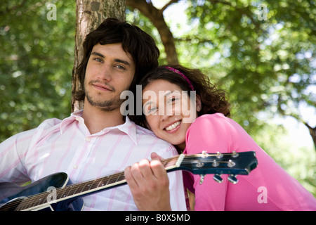 Ein junges Paar sitzt unter einem Baum und Gitarre Stockfoto