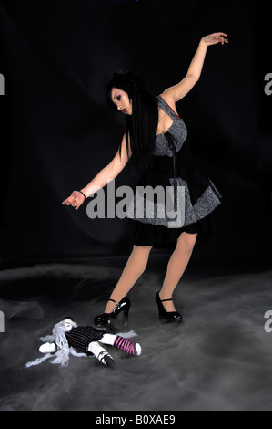 Viktorianische gotische Frau, schöne Raven haired gothic Vampir Mädchen in einem schwarzen und grauen Kleid, tanzen über eine Puppe, die Verlegung auf die Stockfoto