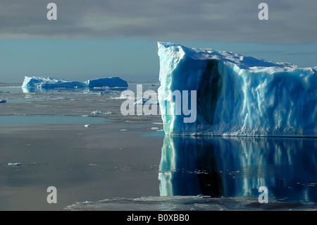 Eine Seite eines blauen antarktischen Eisberges im südlichen Ozean auf einem fast flachen Meer bedeckt von Eisschollen, Antarktis, Südlicher Ozean Stockfoto